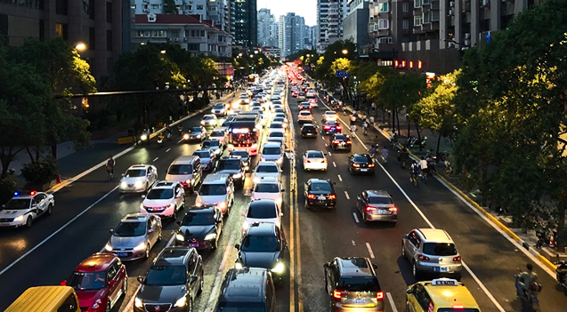 Busy city street with multiple lanes of slow-moving cars and trees lining the road.